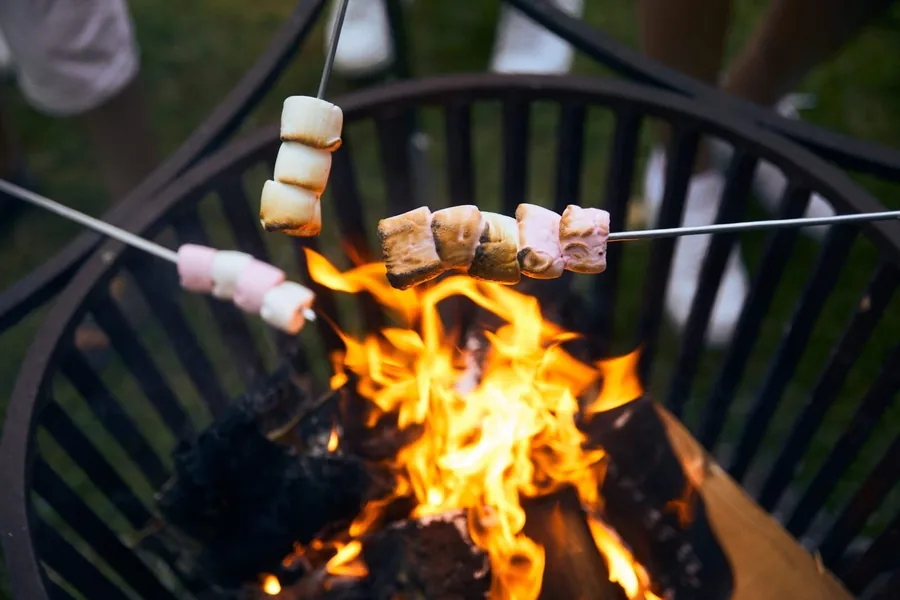 Marshmallows en broodjes aan een spies boven een brandende vuurkorf