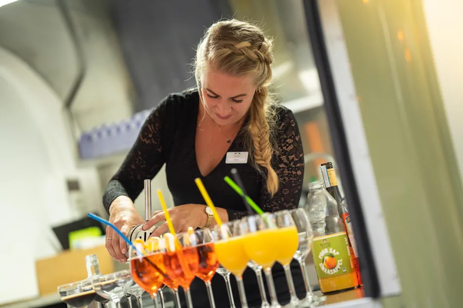 Een medewerkster zet een rij cocktails klaar op de bar