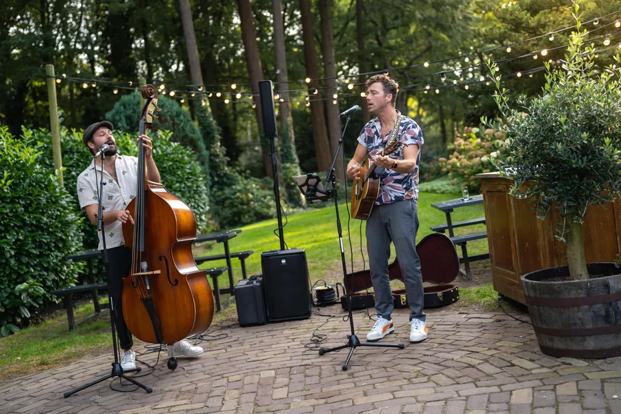 Twee muzikanten met contrabas en gitaar spelen buiten onder de lichtjes