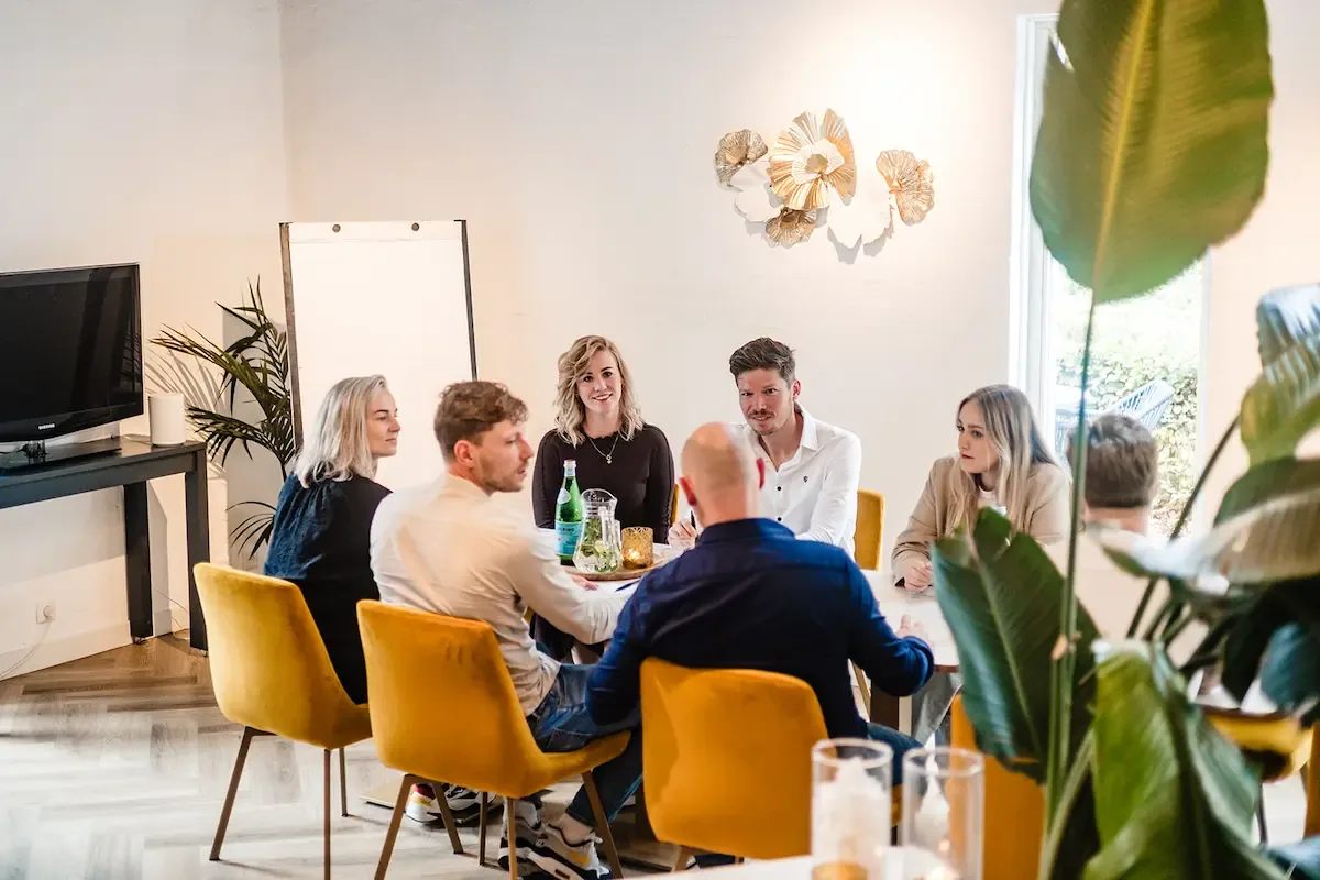 Een groep mensen vergadert rond een tafel met gele fluwelen stoelen