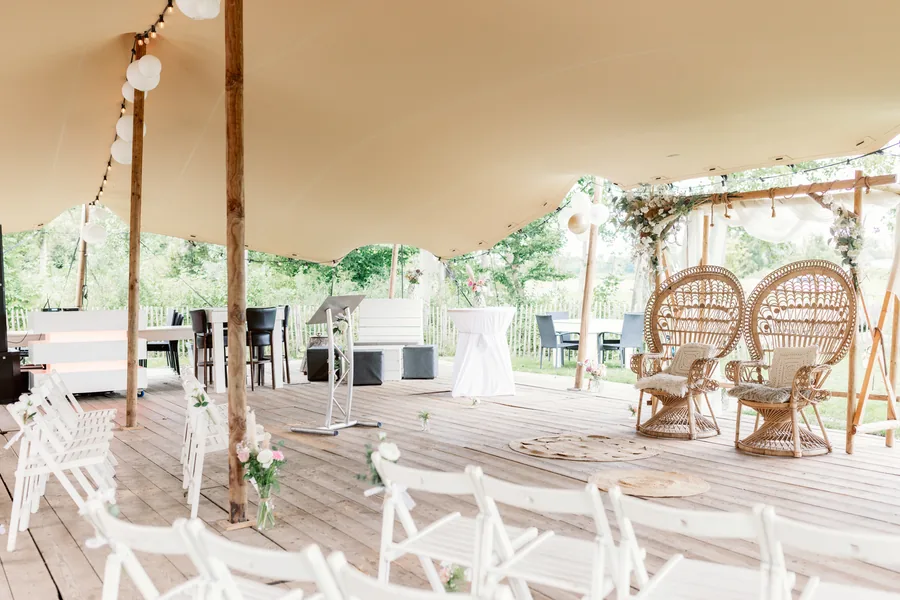 De feesttent van binnen, met rotan stoelen en witte stoelen op een houten vlonder
