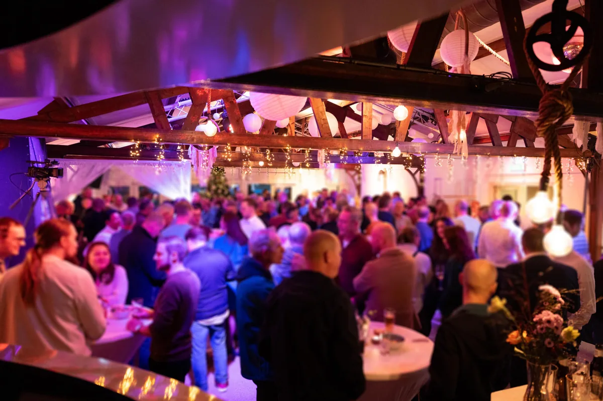 Een druk feest in de zaal van Breezze onder paars licht en lampionnen