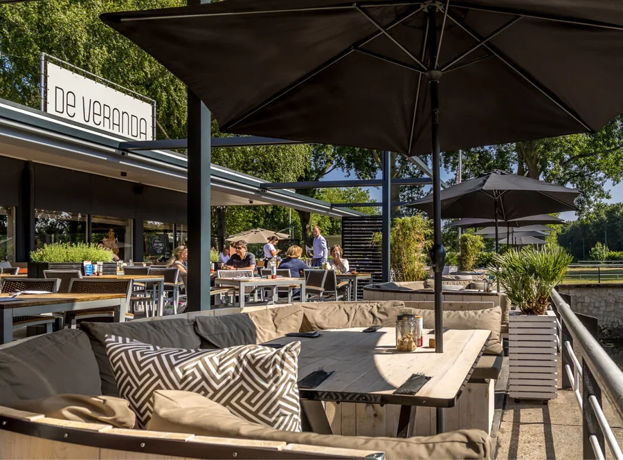 Het terras van De Veranda met parasols en loungebanken aan het water