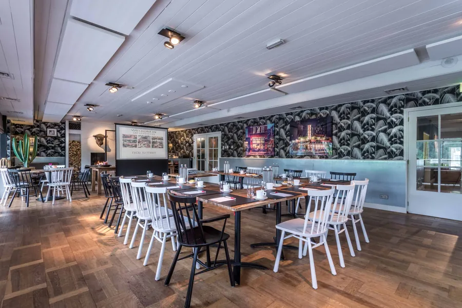 Een zaal met lange tafels en witte stoelen, klaar voor een diner