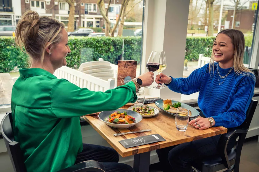 Twee vrouwen proosten met een glas wijn aan een tafel op het terras van De Veranda