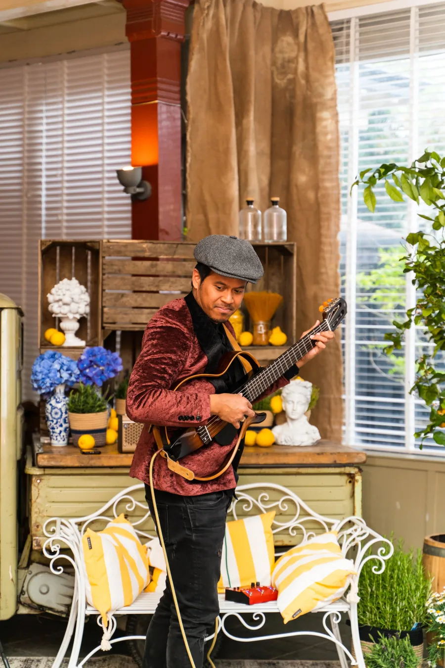 Een muzikant speelt gitaar in een hoek van de zaal, tussen bloemen en kratten