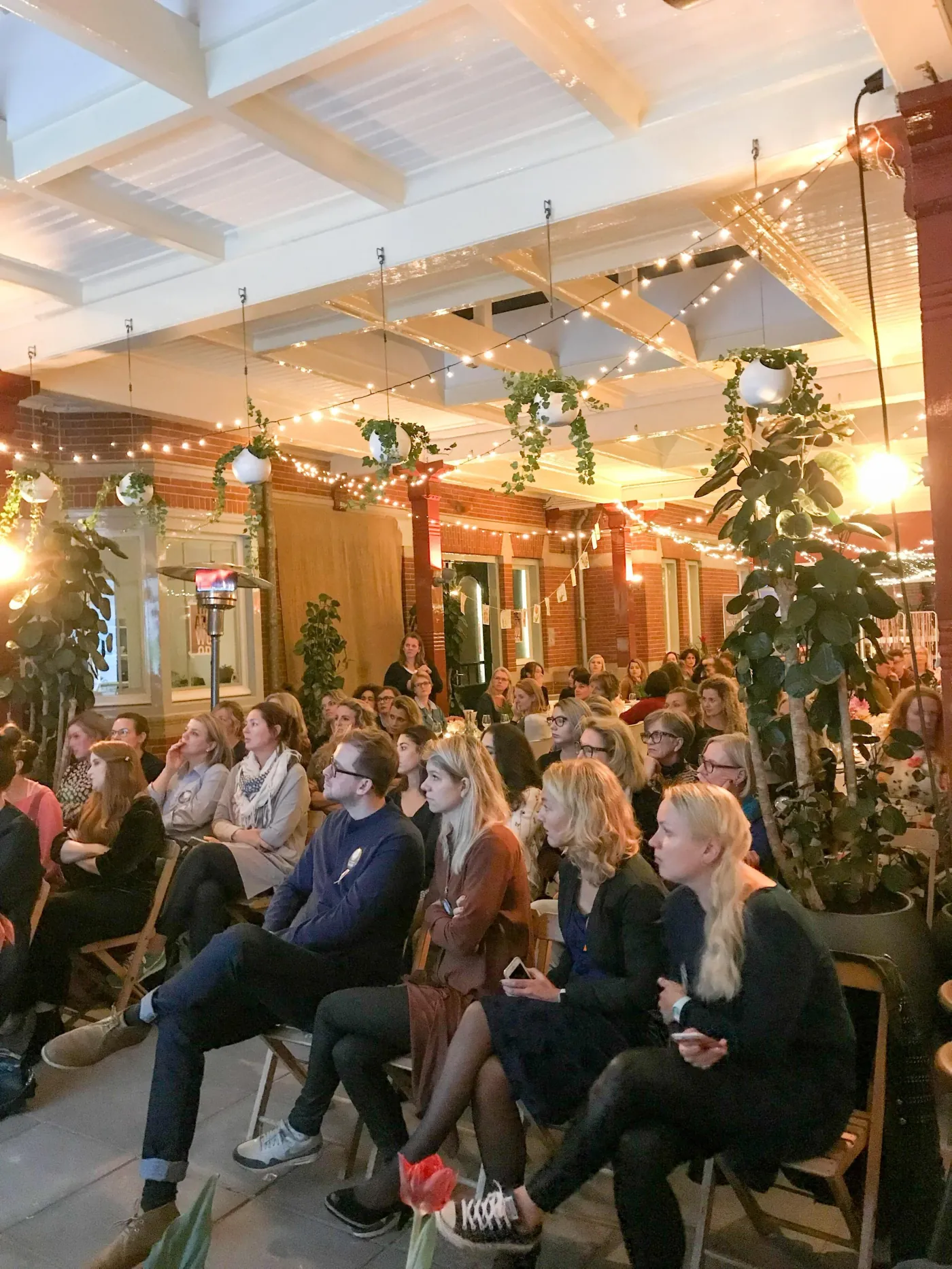 Publiek zit dicht op elkaar in de zaal onder de lichtjes en het groen