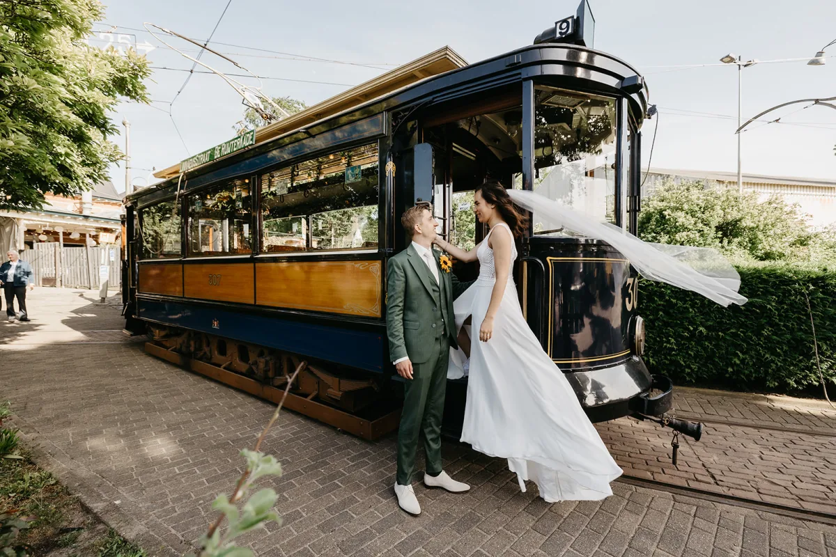 Een bruidspaar staat naast de historische tram die op de kop van de Amstelveenseweg is voorgereden