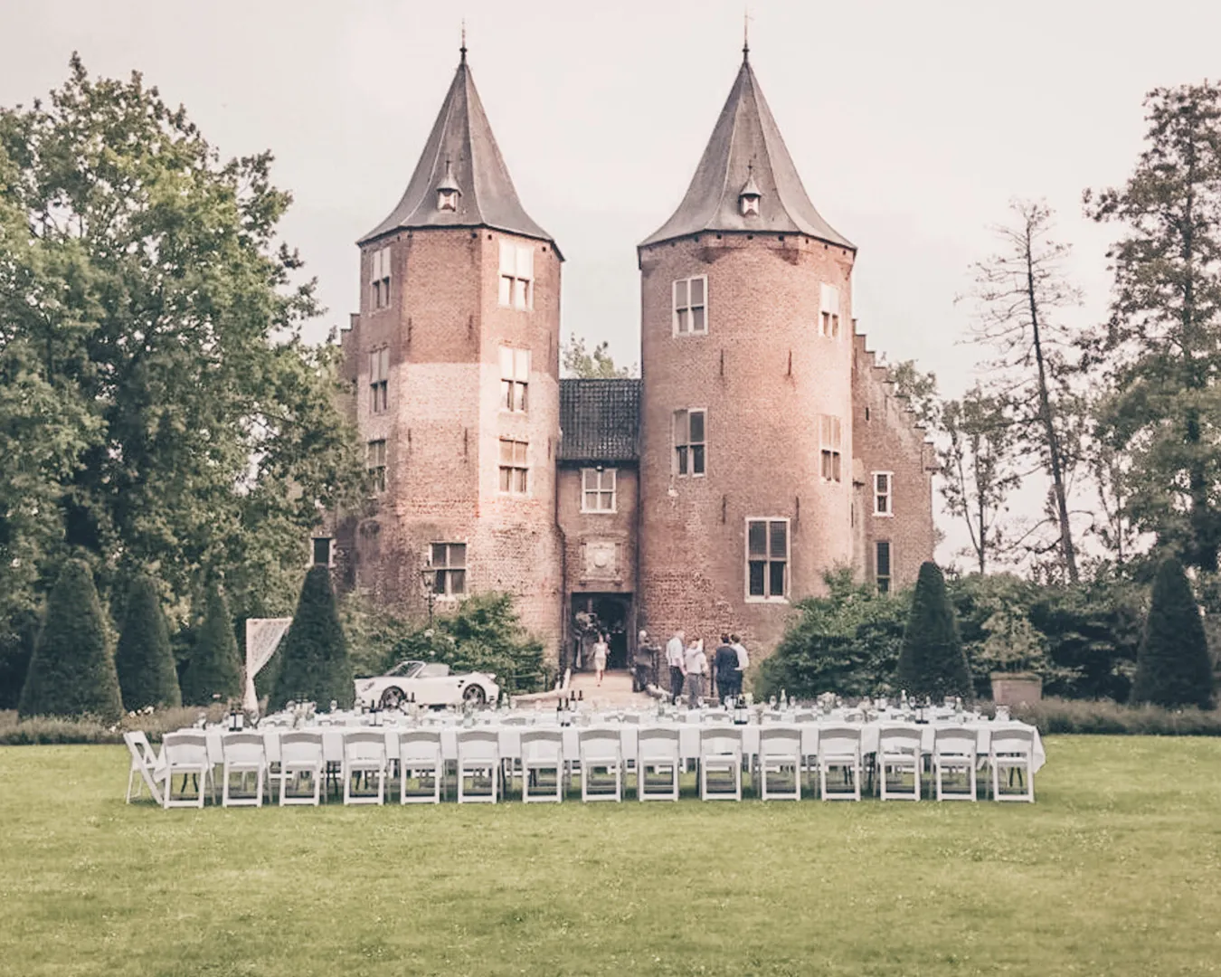Kasteel Dussen met zijn twee ronde torens, met rijen witte stoelen op het gazon ervoor