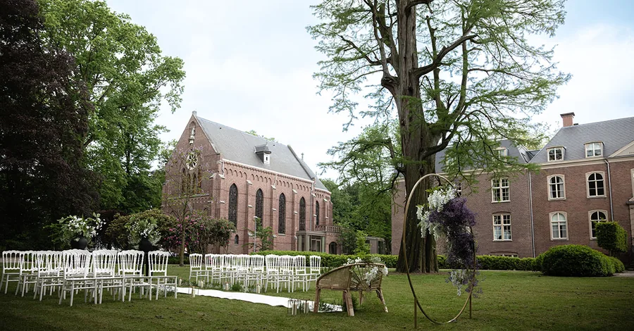 De kapel van Kasteel Bijstervelt met witte stoelen en een bloemenboog in de tuin