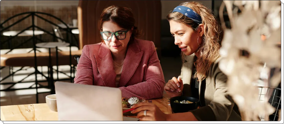 Twee vrouwen kijken samen naar een laptop aan een tafel in een eventlocatie